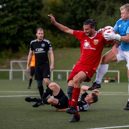Das Bild zeigt den Torwart und einen Gegenspieler im Zweikampf. Hinter ihnen liegt ein weiterer Akteur am Boden.