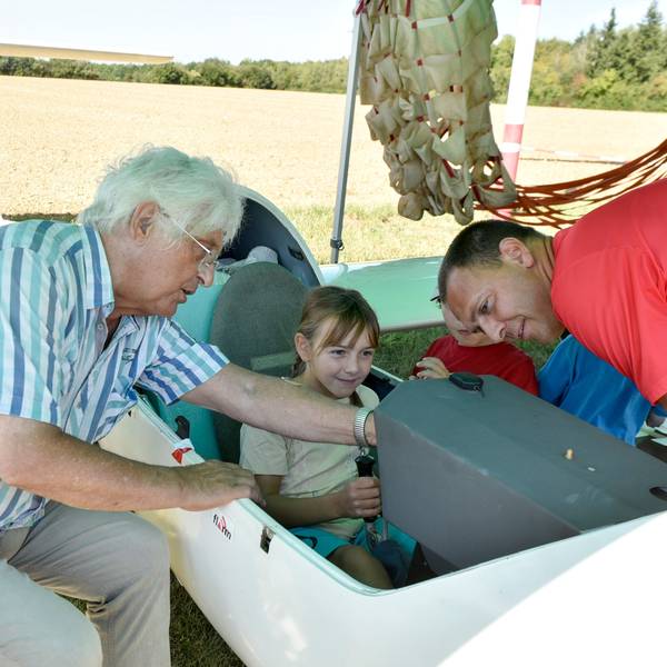 Das Bild zeigt ein junges Mädchen im offenen Cockpit. Links und rechts von ihr erklären die beiden Herren die Instrumente.