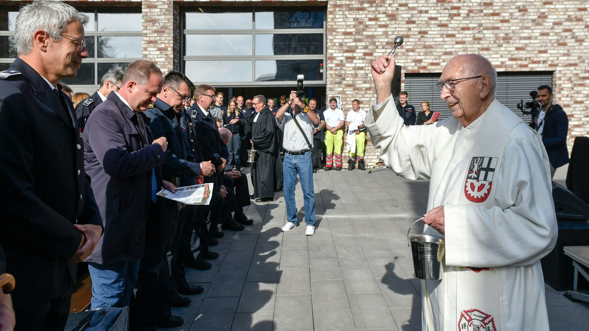 Auf dem Bild ist ein Pfarrer zu sehen, der Reihen von Gästen mit Weihwasser besprüht.