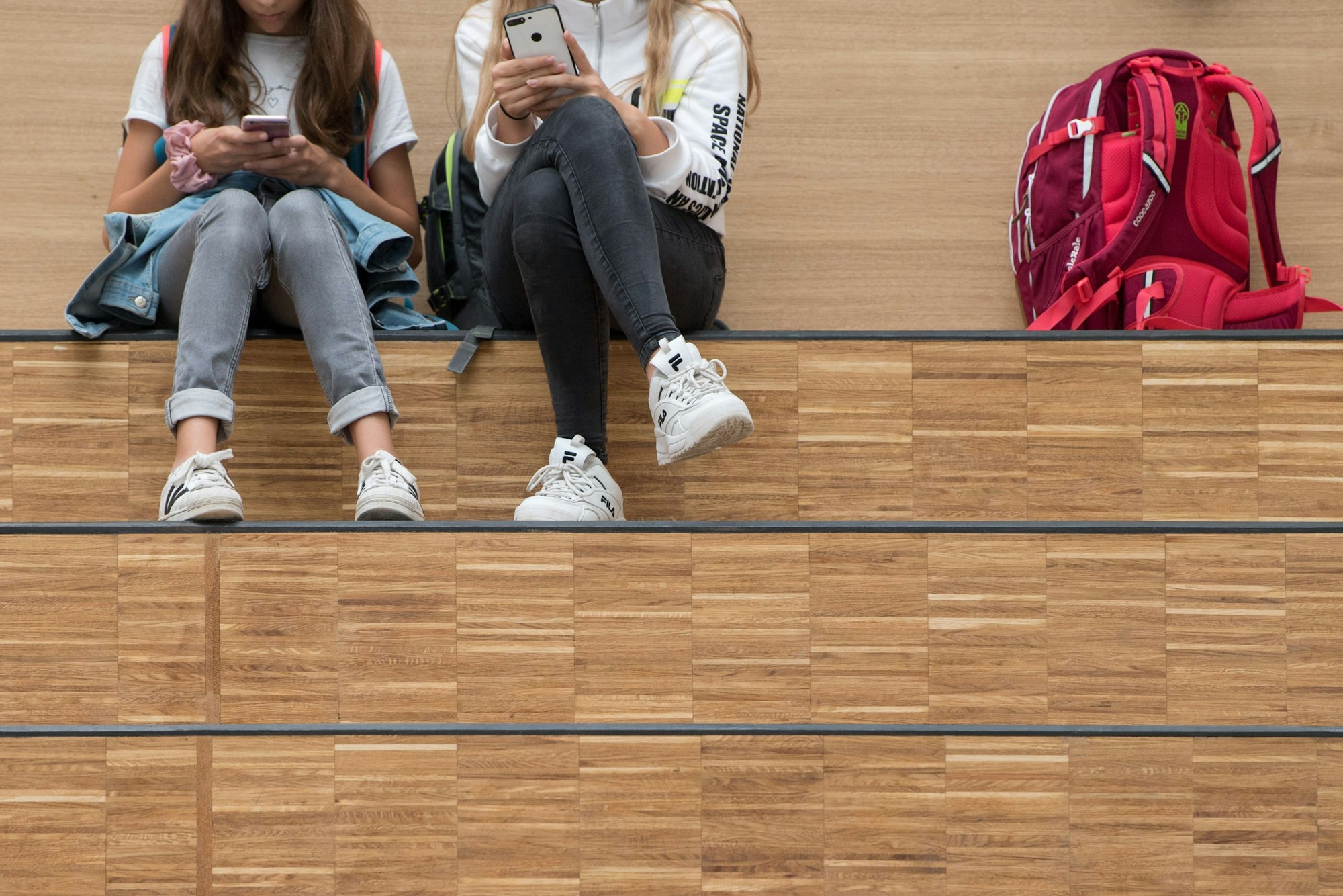 Schülerinnen sitzen im Foyer eines Gymnasiums auf einer Freitreppe und halten jeweils ein Smartphone.