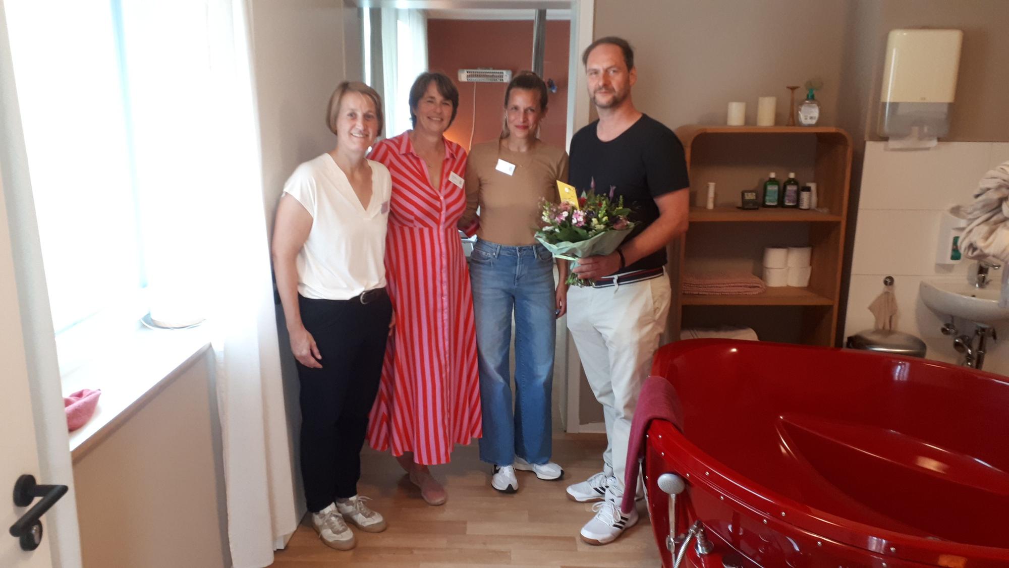 Drei Frauen und ein Mann stehen in Räumlichkeiten eines Geburtshauses. Der Mann hält einen Blumenstrauß.