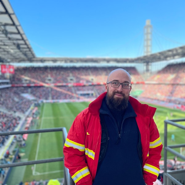 Auf dem Bild ist ein Mann in DLRG-Uniform auf der Tribüne des Rhein-Energie-Stadions zu sehen.