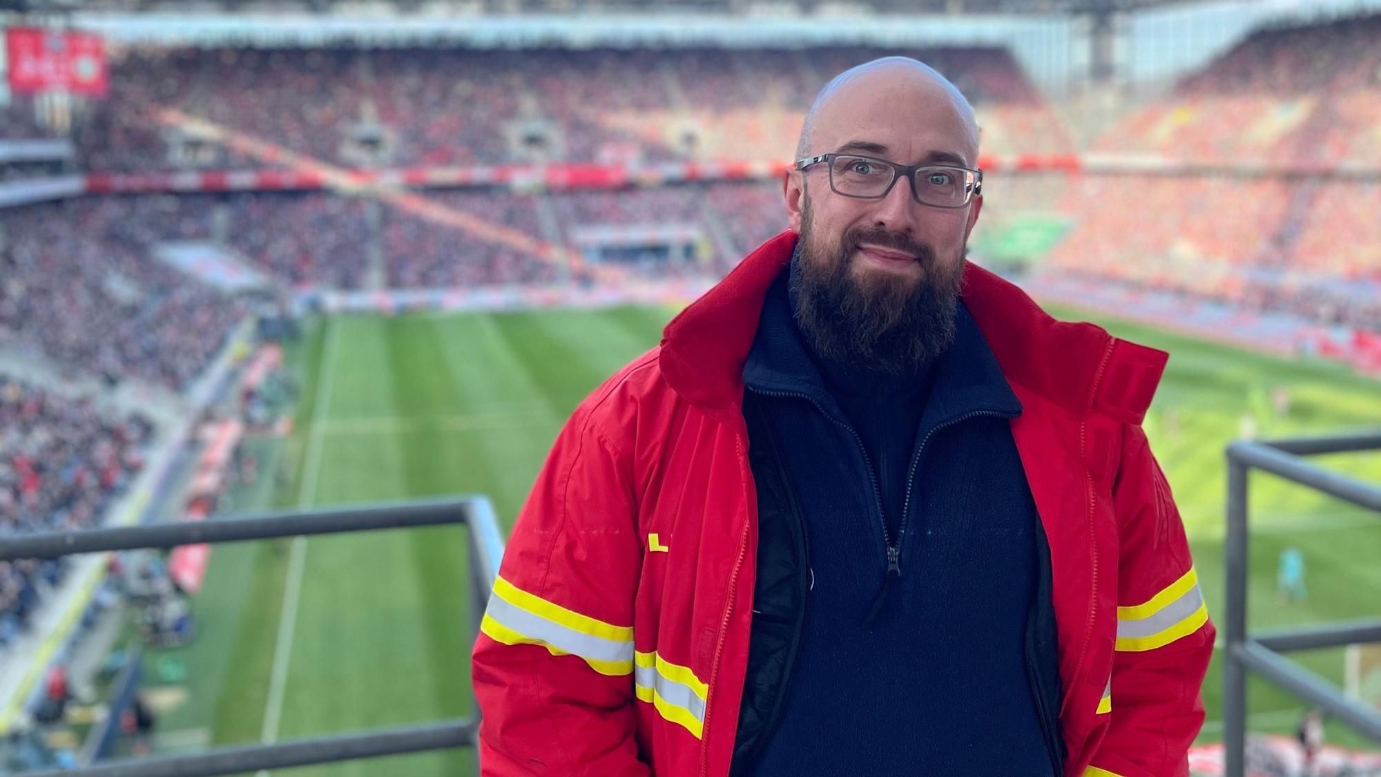 Auf dem Bild ist ein Mann in DLRG-Jacke in einem Fußballstadion zu sehen.