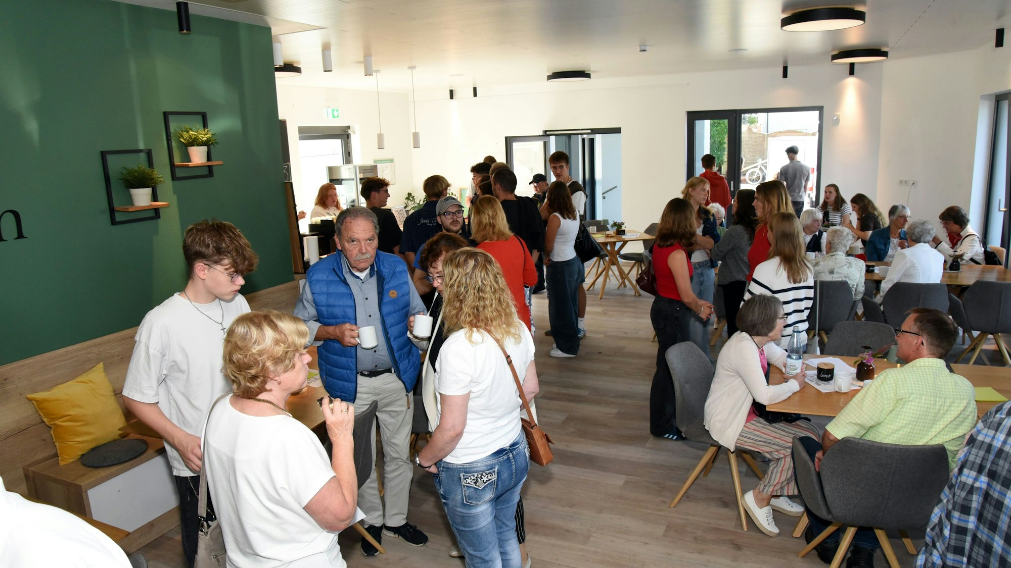 Menschen an Tischen und im Stehen in einem Speisesaal.