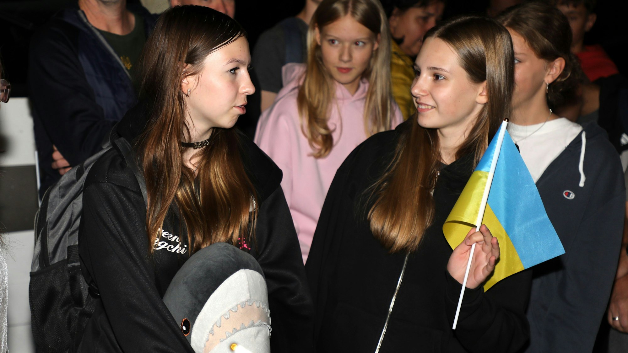 Zwei Mädchen stehen mit einer Ukrainefahne und Gepäck in der Nacht zu Montag (8. September) an der Integrierten Gesamtschule Paffrath.