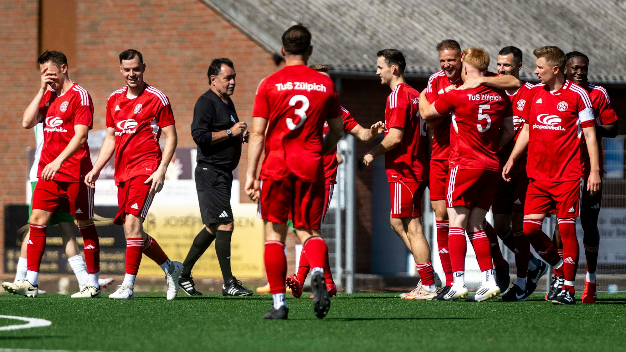 Zülpicher Spieler jubeln nach dem frühen 1:0. Ein Spieler am linken Bildrand hält sich ungläubig die Hand vors Gesicht. Der Schiedsrichter spricht mit den Spielern.