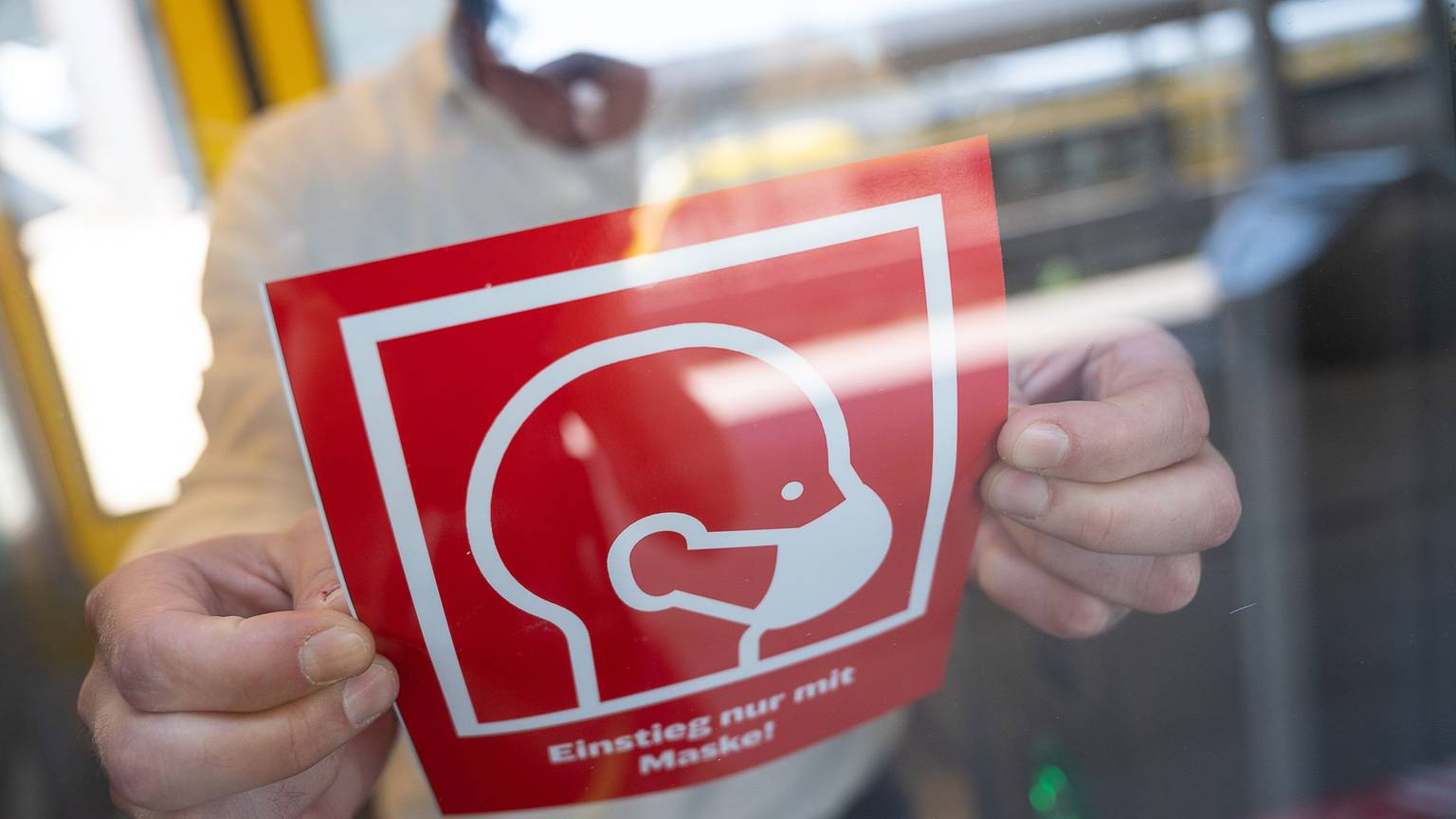 ARCHIV - 07.08.2020, Baden-Württemberg, Stuttgart: Ein Mann bringt während eines Pressetermins, bei dem neue Hinweistafeln zur Maskenpflicht in Zügen und Bahnhöfen vorgestellt werden, einen der Hinweise, auf dem «Einstieg nur mit Maske» steht, an einem Zug an.