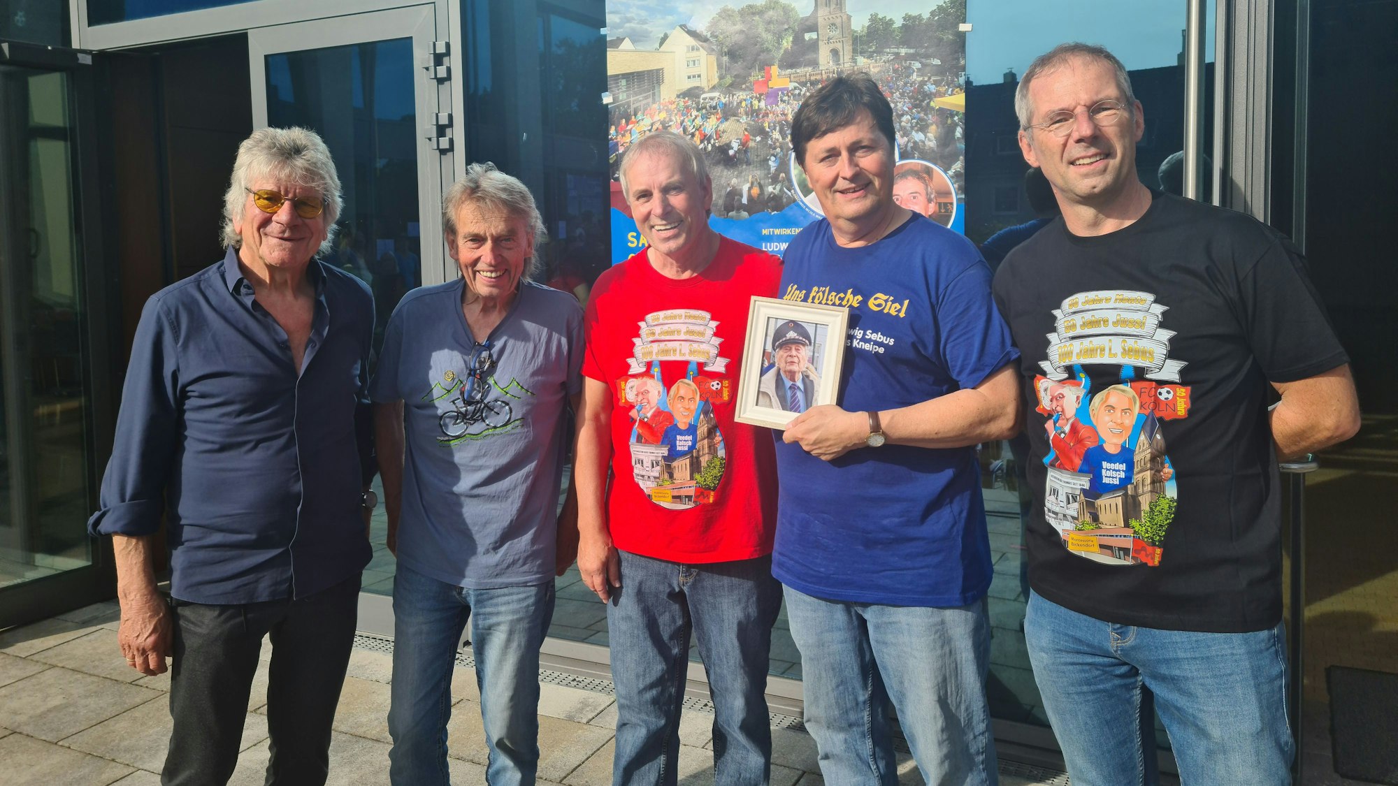 Fünf Männer stehen vor einer Glastür. Einer hält ein Bild.