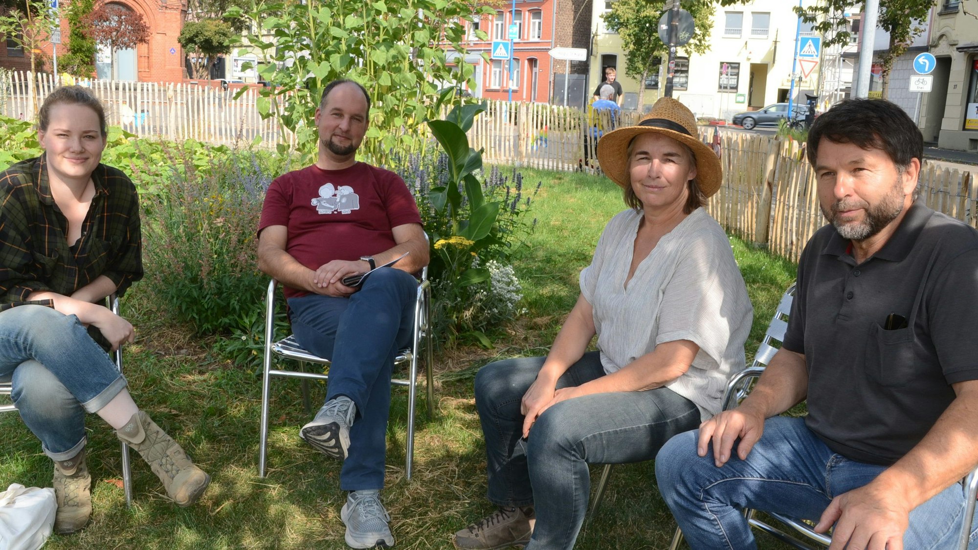 Zwei Männer und zwei Frauen sitzen im Schatten eines Baumes in einem Garten.