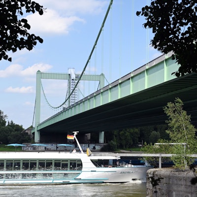 Ein Ausflugsschiff fährt unter einer grünen Hängebrücke her.