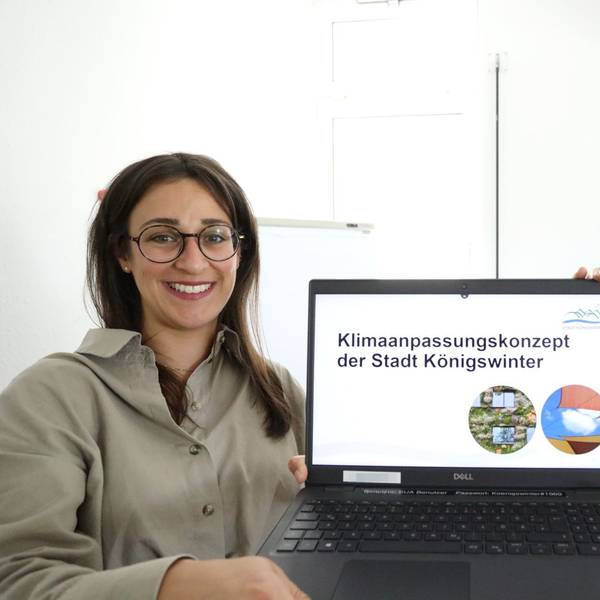 Zwei junge Frauen halten einen Laptop, auf dessen Monitor der Schriftzug „Klimaanpassungskonzept der Stadt Königswinter“ steht.