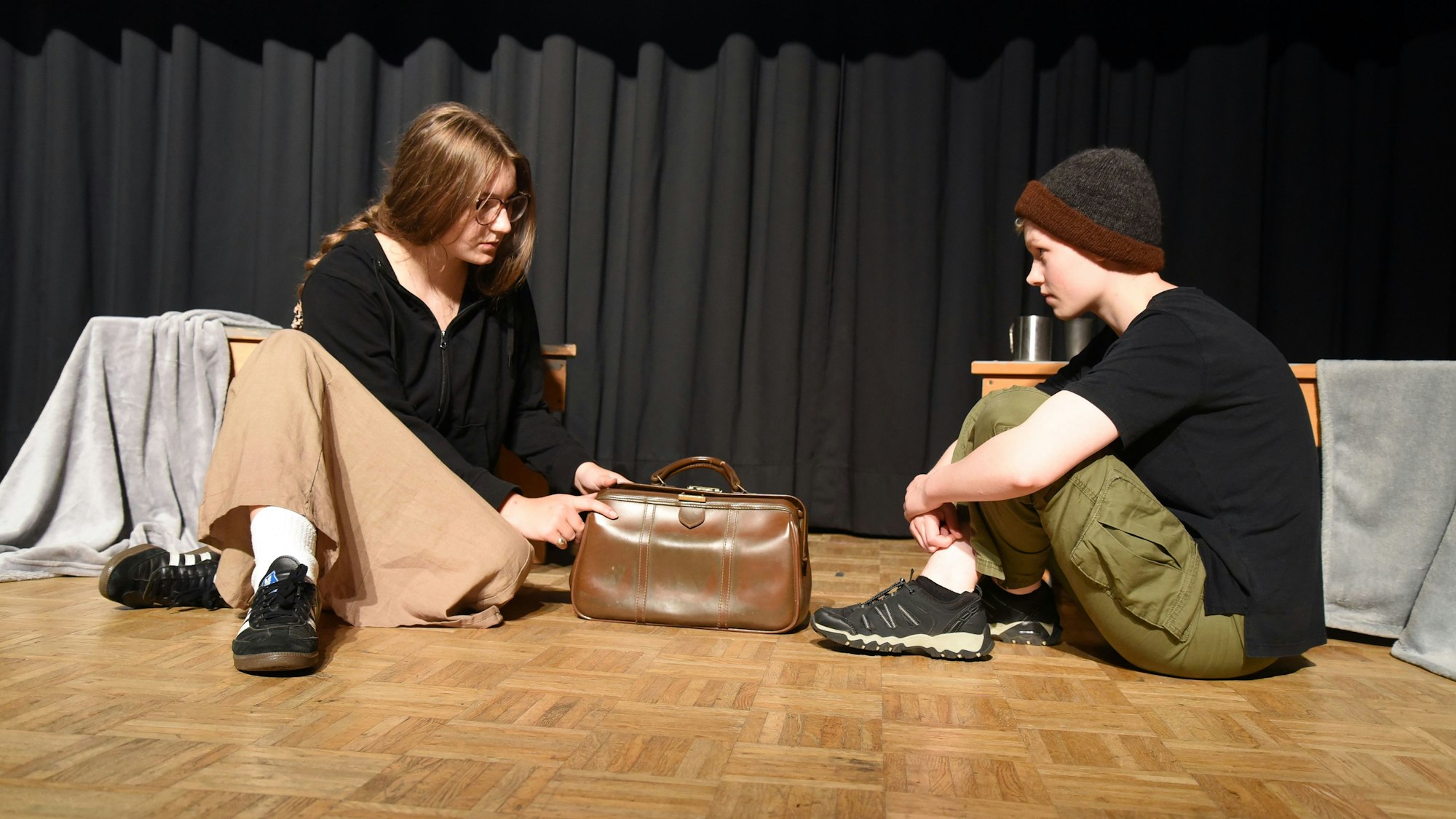 Zwei junge Leute sitzen auf dem Boden und sehen sich an.