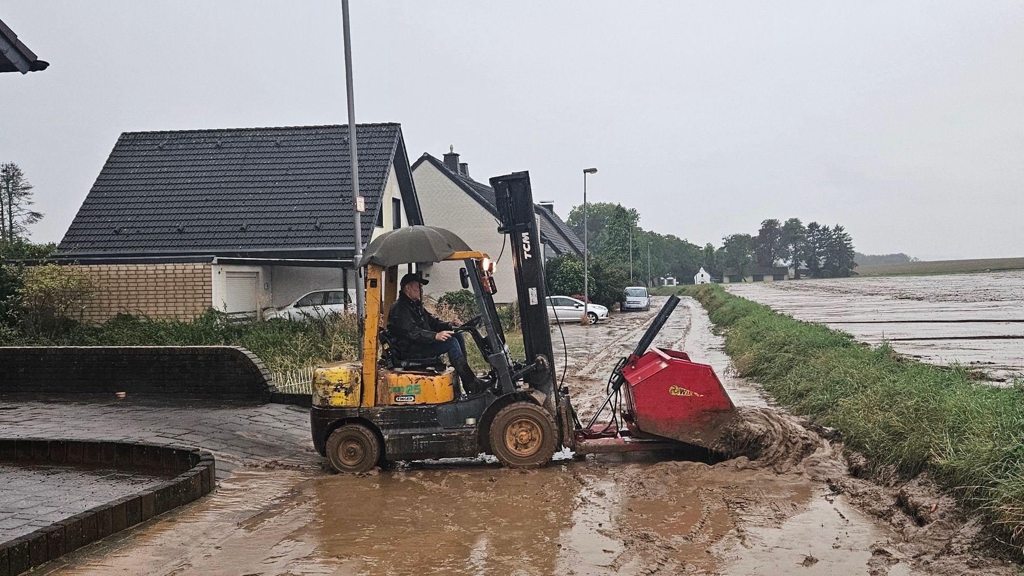 Zu sehen ist, wie ein Mann mit einem Gabelstapler Schlamm von einer Straße schiebt.