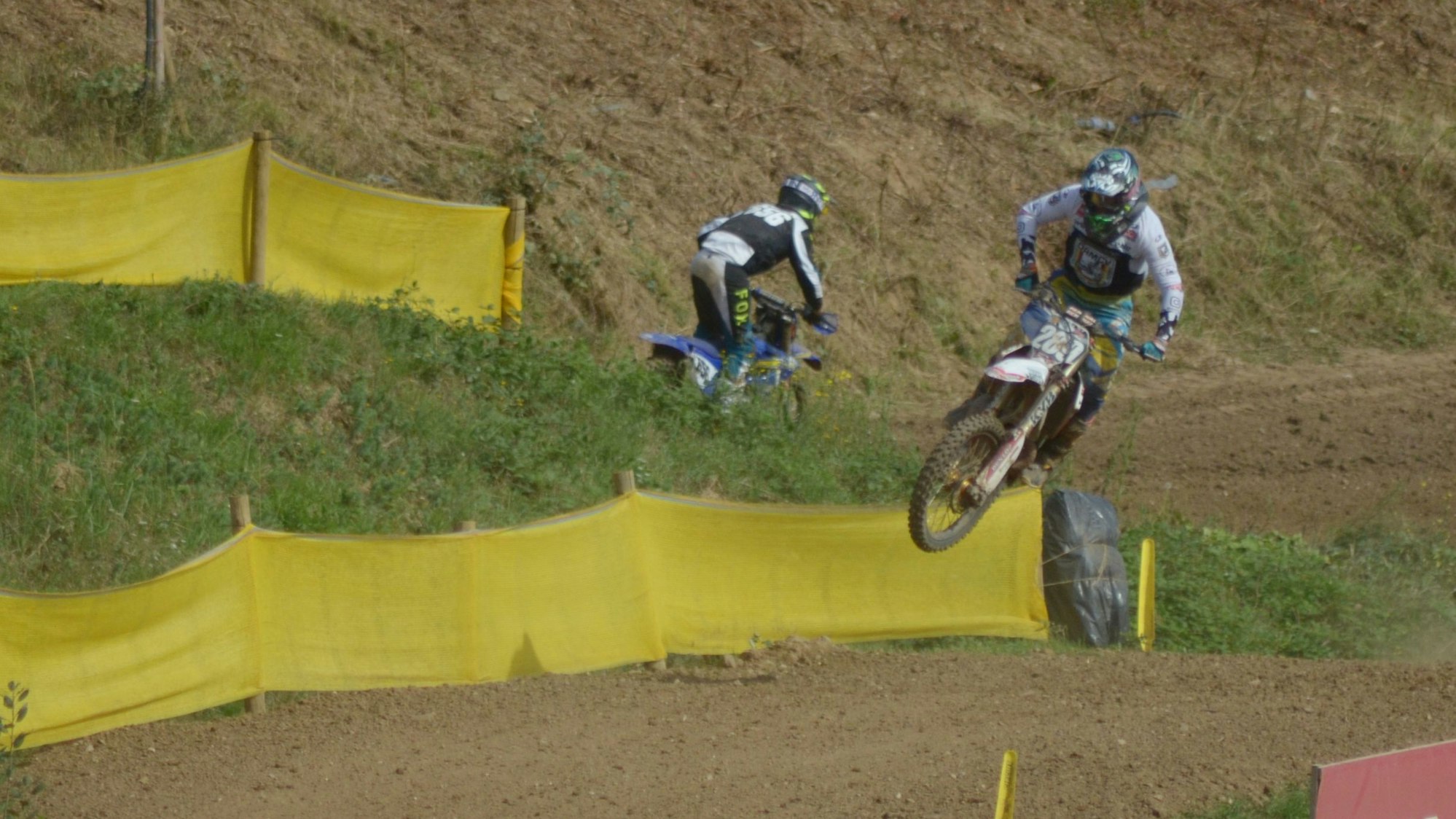 Ein Motocrossfahrer hat mit seiner Maschine abgehoben. Im Hintergrund ist ein weiterer Starter zu sehen.