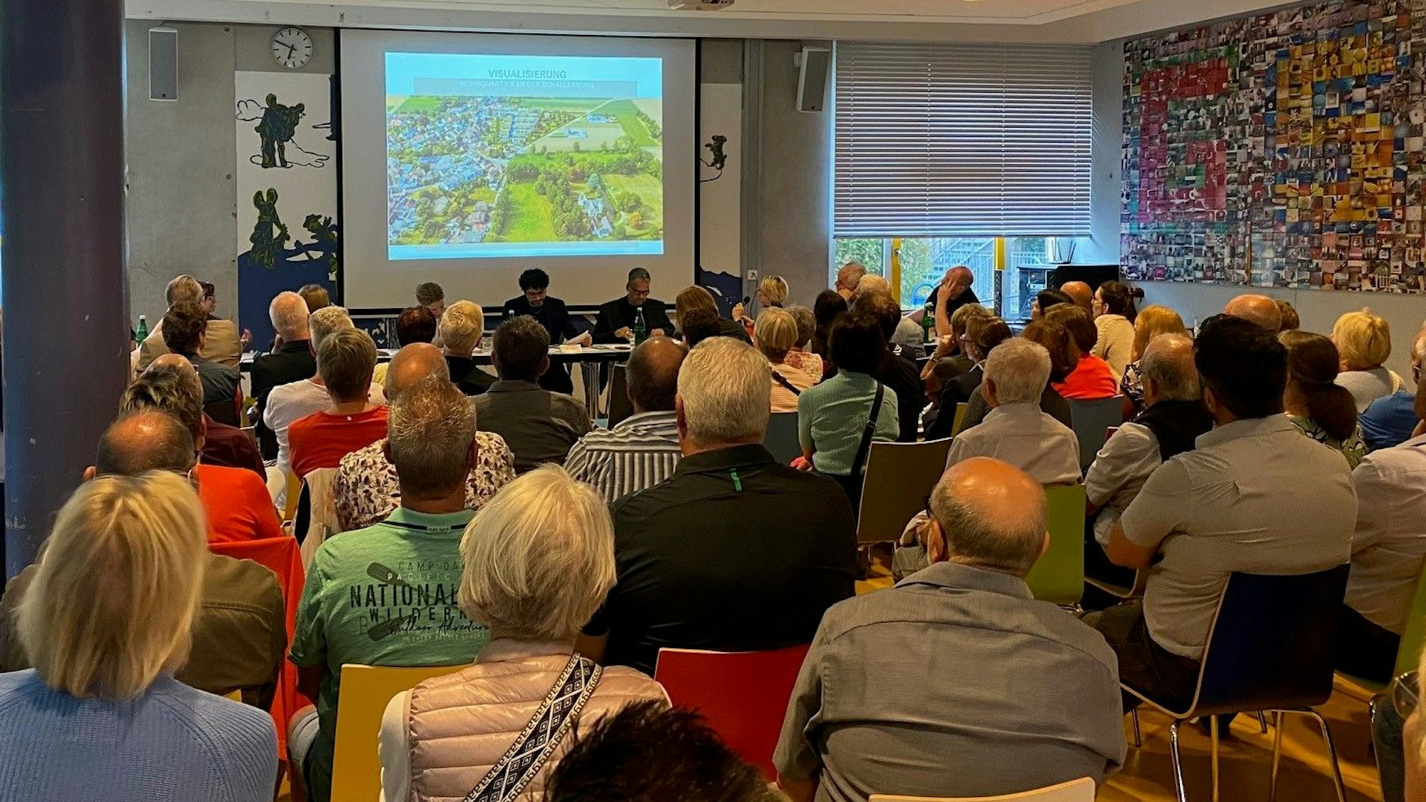 Zu sehen sind Menschen, die auf Stühlen sitzen und eine Präsentation verfolgen.