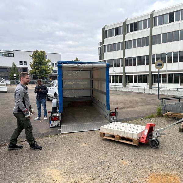 Das Foto zeigt, wie vor dem AOK-Gebäude Steine auf einer Palette mit dem Hubwagen auf einen Anhänger verladen werden.