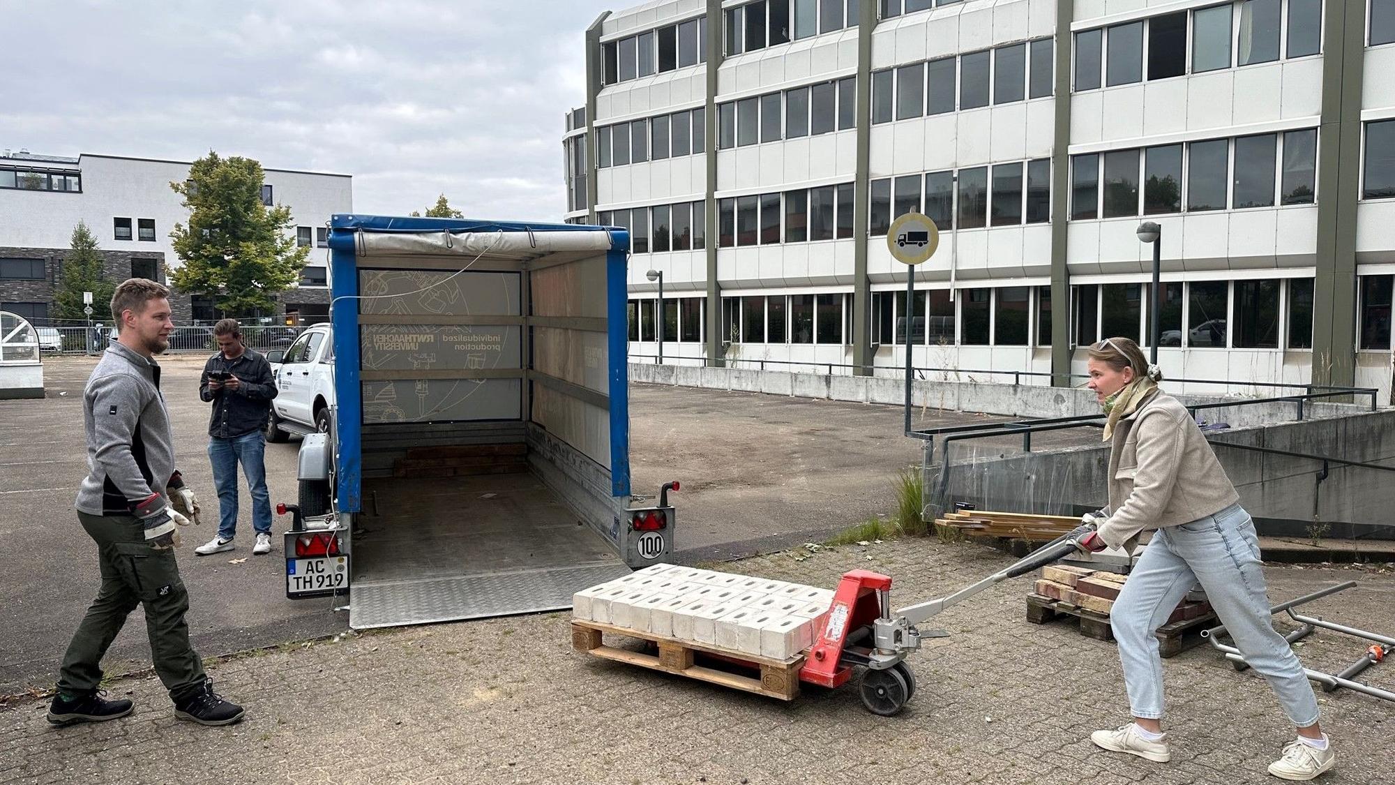 Das Foto zeigt, wie vor dem AOK-Gebäude Steine auf einer Palette mit dem Hubwagen auf einen Anhänger verladen werden.