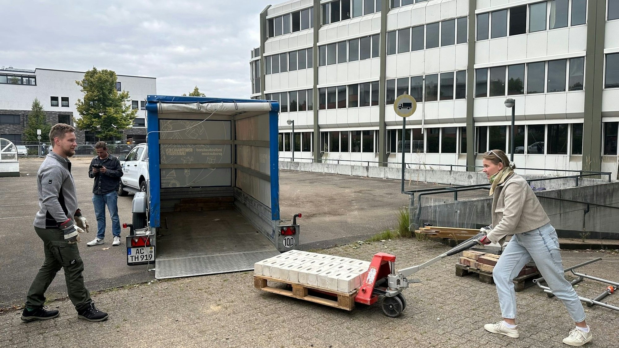 Das Foto zeigt, wie vor dem AOK-Gebäude Steine auf einer Palette mit dem Hubwagen auf einen Anhänger verladen werden.