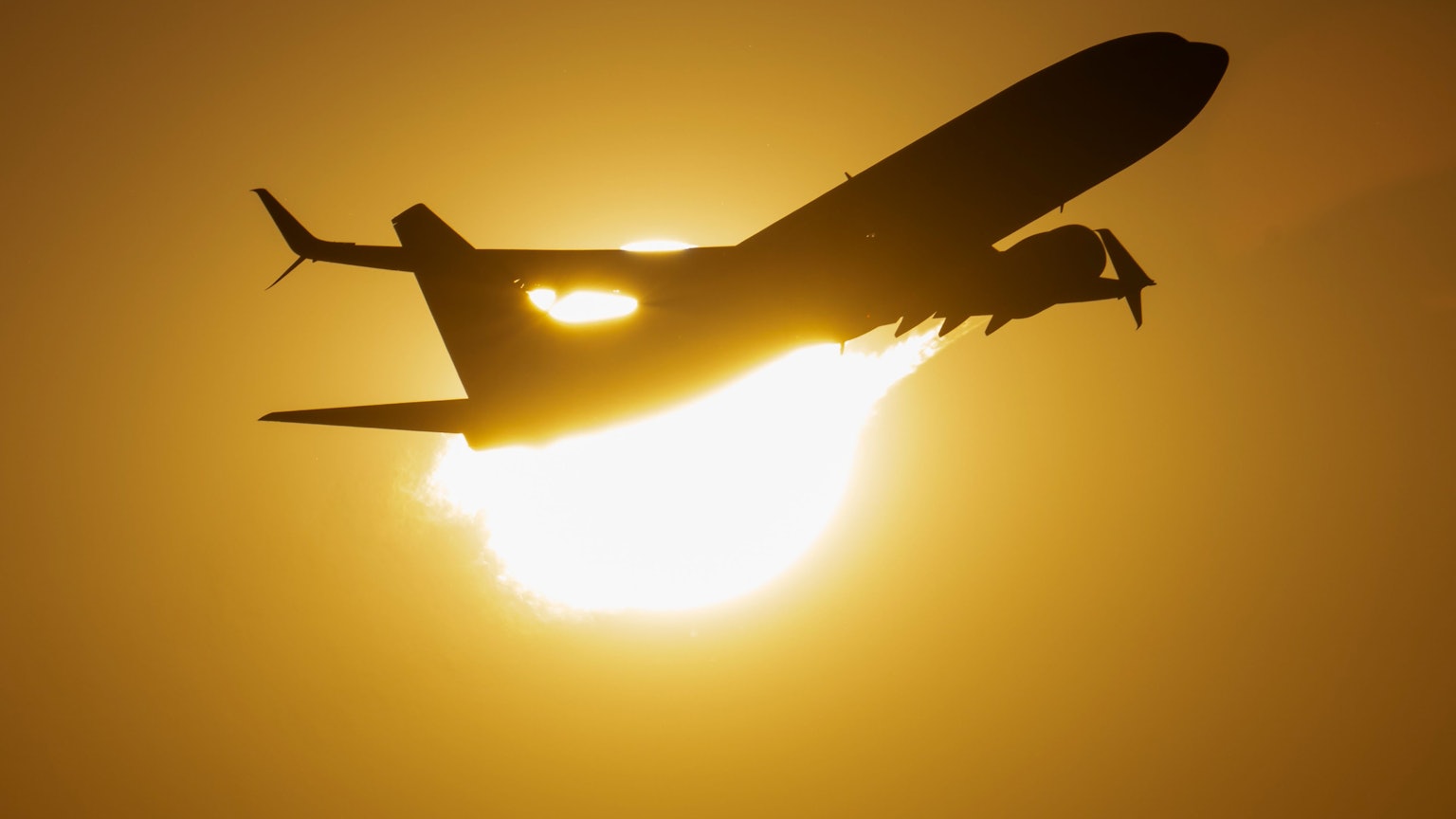 Ein Flugzeug fliegt an der untergehenden Sonne vorbei.