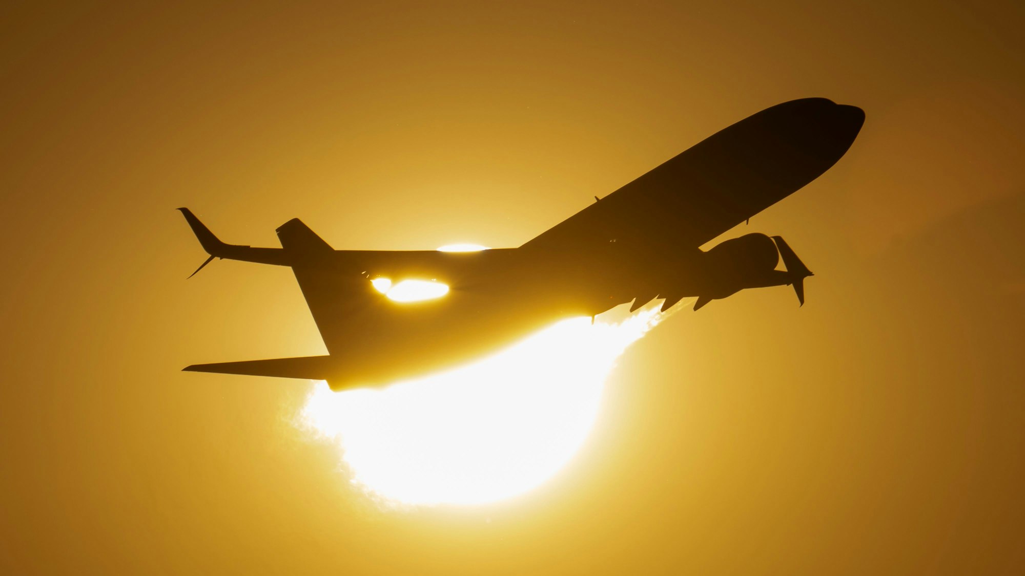 Ein Flugzeug fliegt an der untergehenden Sonne vorbei.