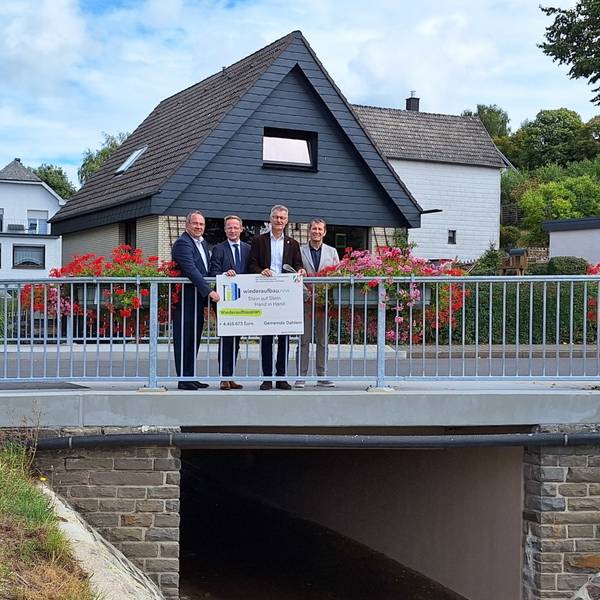 Vier Männer stehen auf einer Brücke und halten einen symbolischen Scheck.
