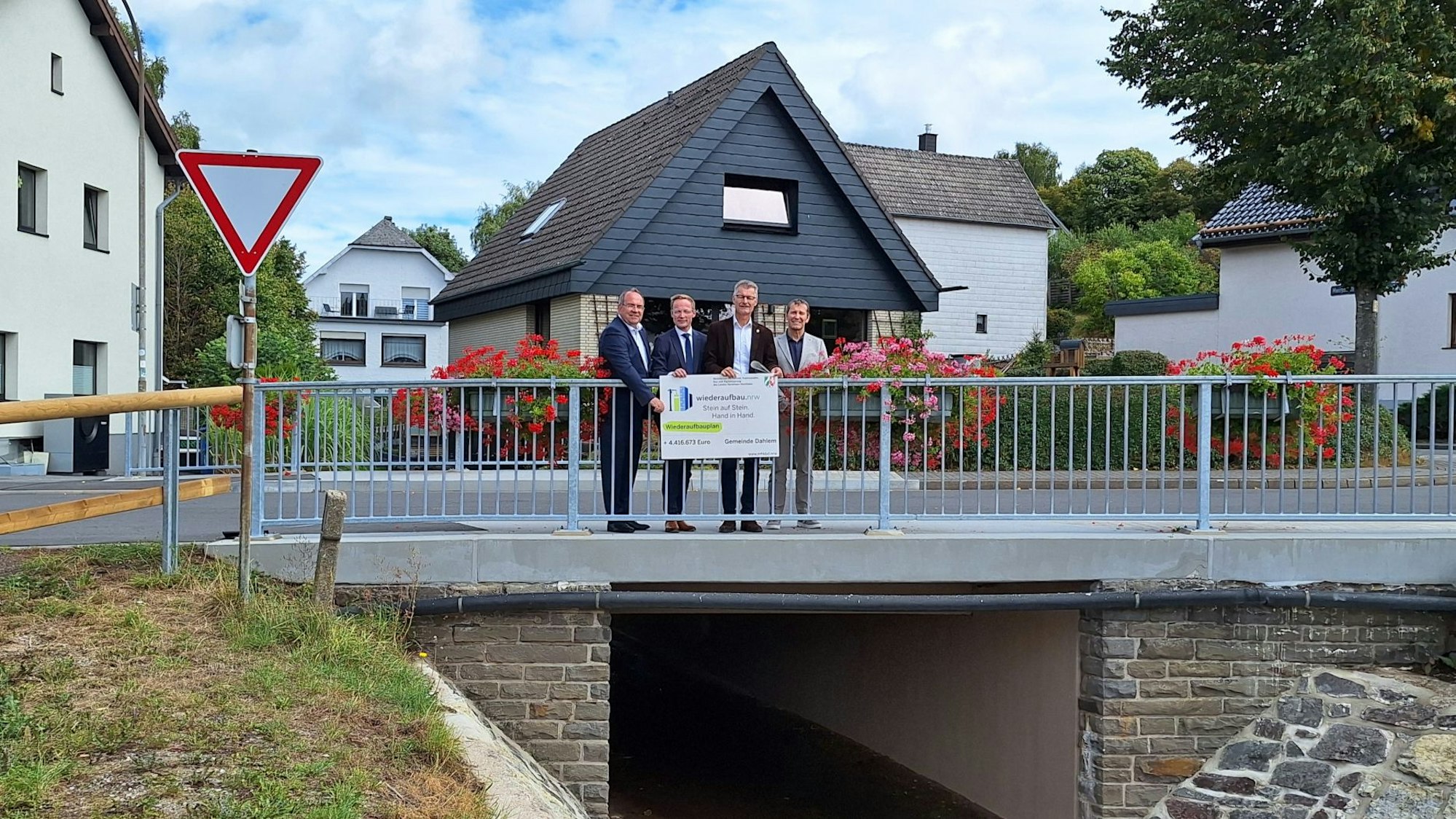 Vier Männer stehen auf einer Brücke und halten einen symbolischen Scheck.