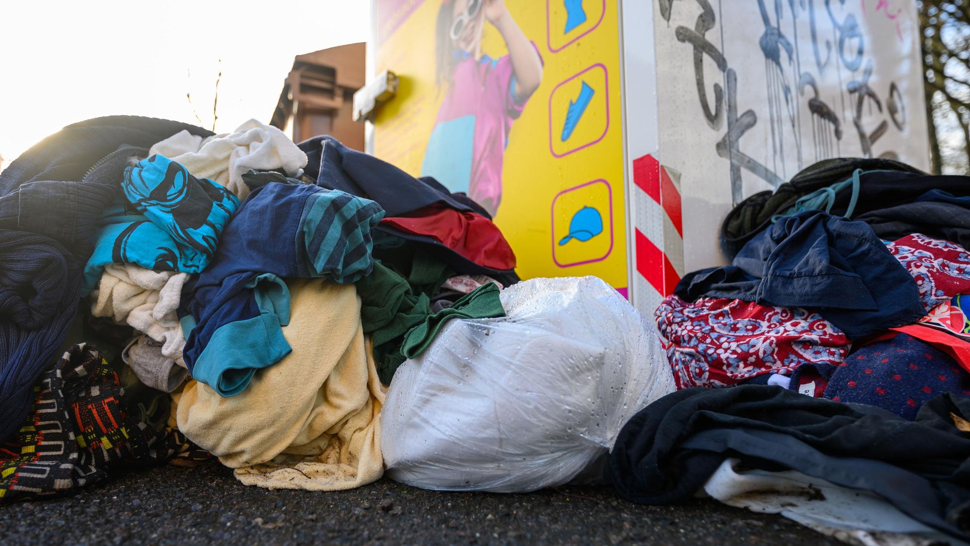 Gebrauchte Kleidungsstücke liegen vor einem Sammelcontainer für Altkleider.