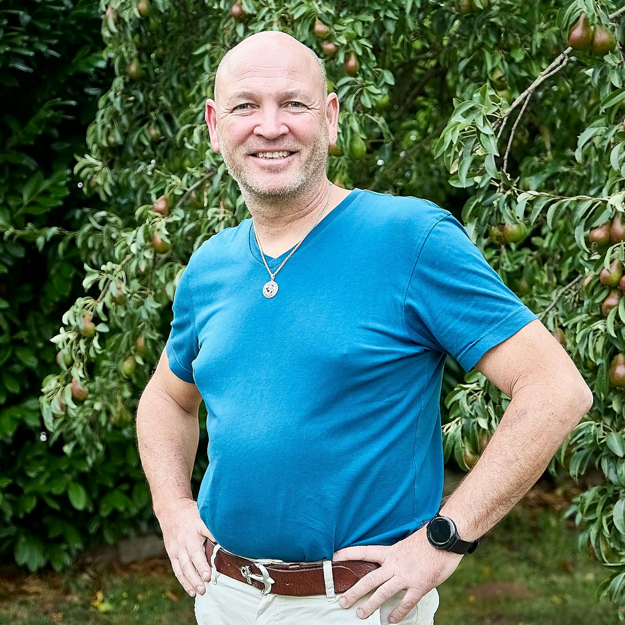 Dirk Nagelschmidt hat seine Hände auf die Hüfte gestützt und steht vor einem Obstbaum.