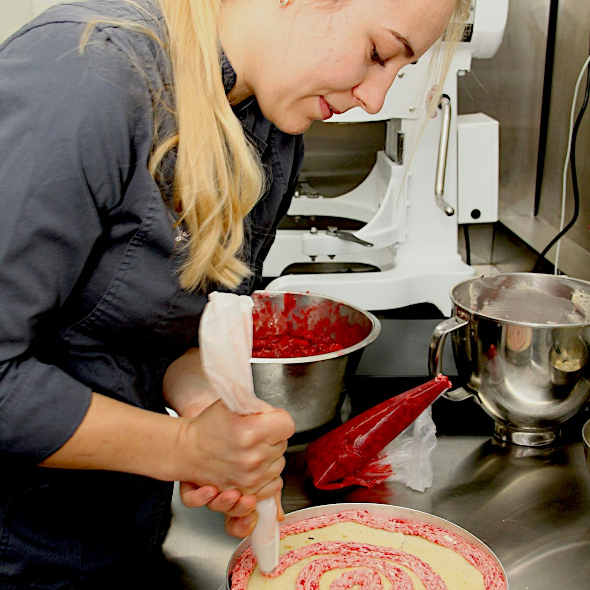 Die junge Konditormeisterin Lisa Sahin steht mit Spritzbeutel in einer Küche und arbeitet an einer Torte.