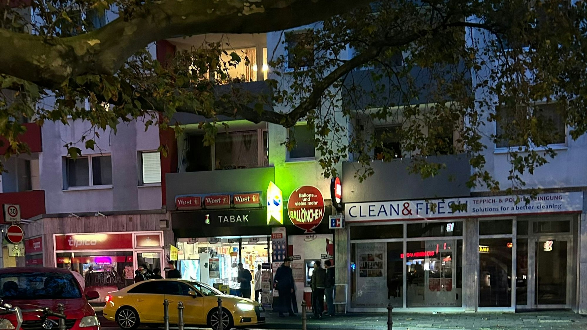 Vor einem hell erleuchteten Kiosk parken abends mehrere Autos.