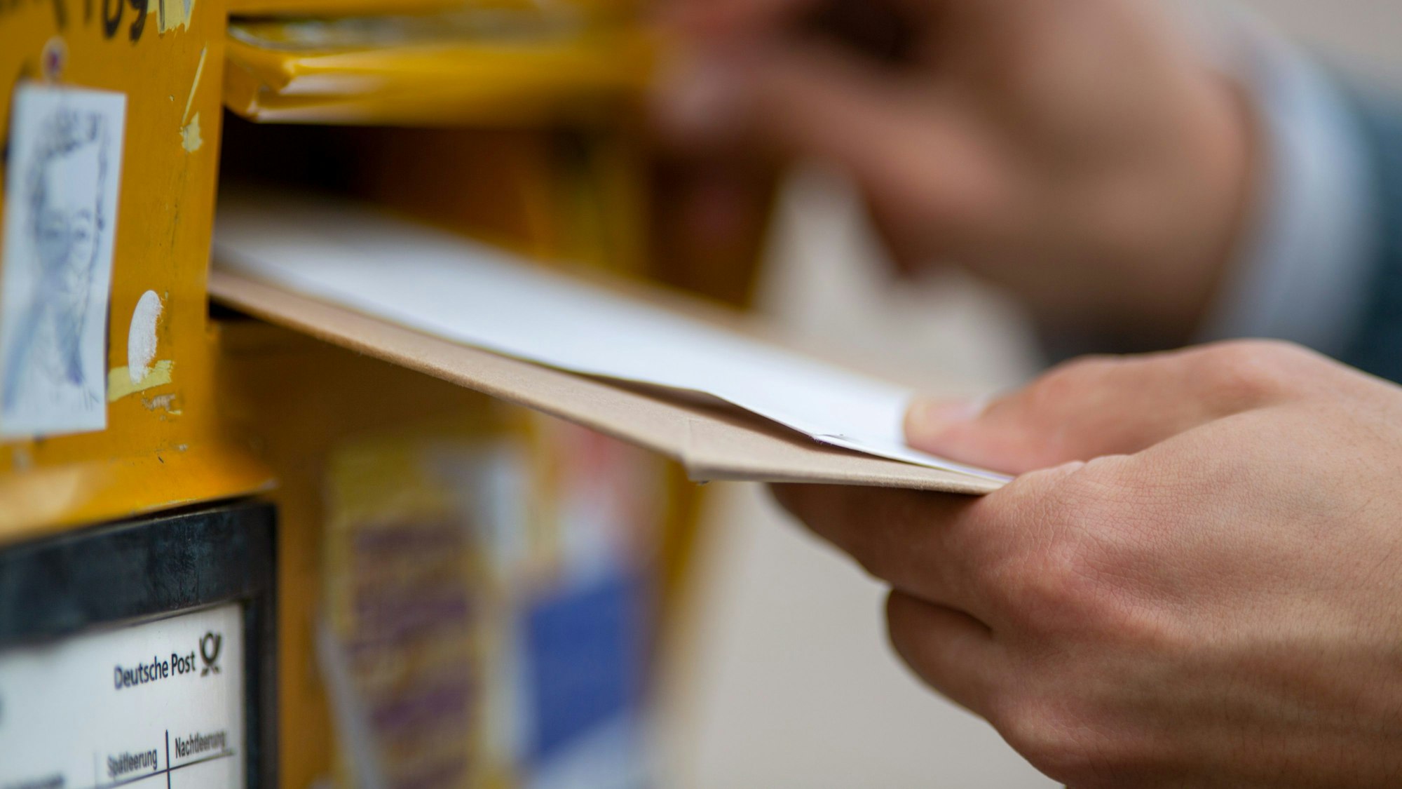 Eine Person wirft einen Brief in einen Briefkasten der Deutschen Post.