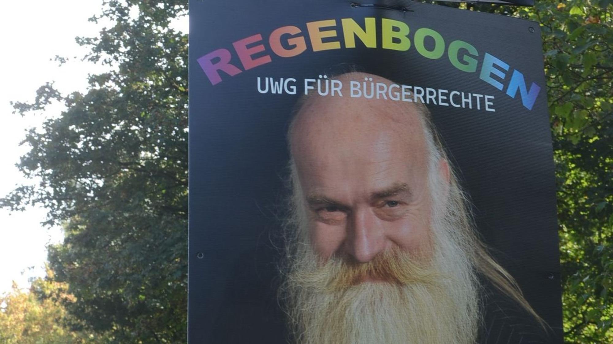 Ein Mann mit langem Bart unter dem Schrifzug Regenbogen UWG für Bürgerrechte.