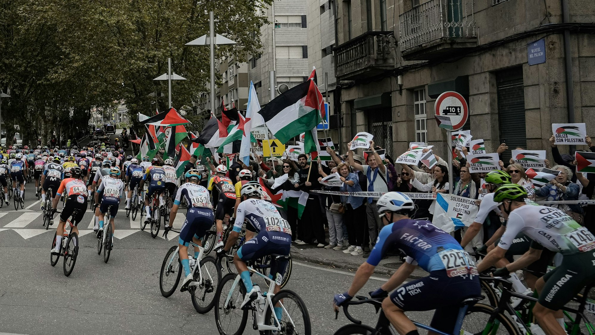 Menschen protestieren mit palästinensischen Fahnen gegen den Gaza-Krieg, als Teilnehmer der Vuelta a España in ein Stadt fahren.