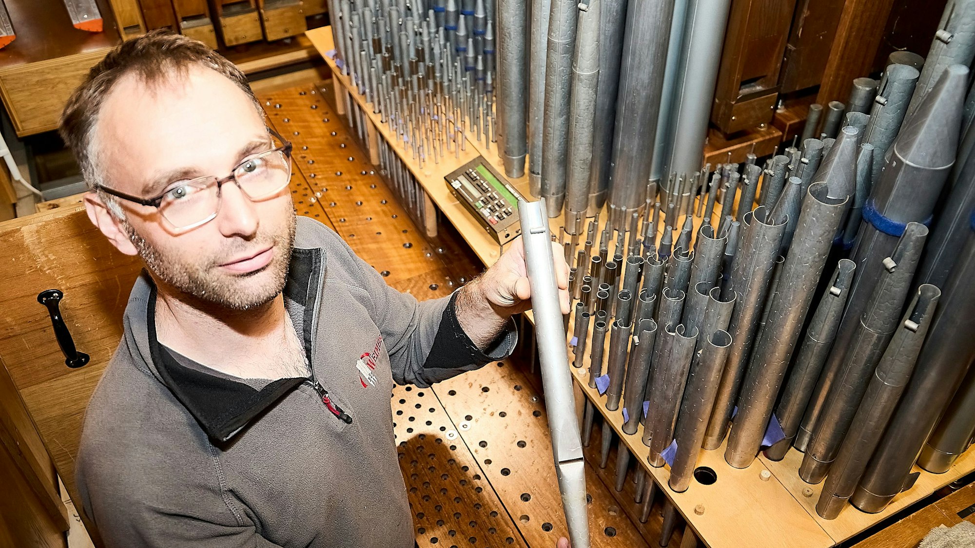 Markus Moutschen hält eine Orgelpfeife in den Händen, dahinter sind zahlreiche Pfeifen zu sehen.