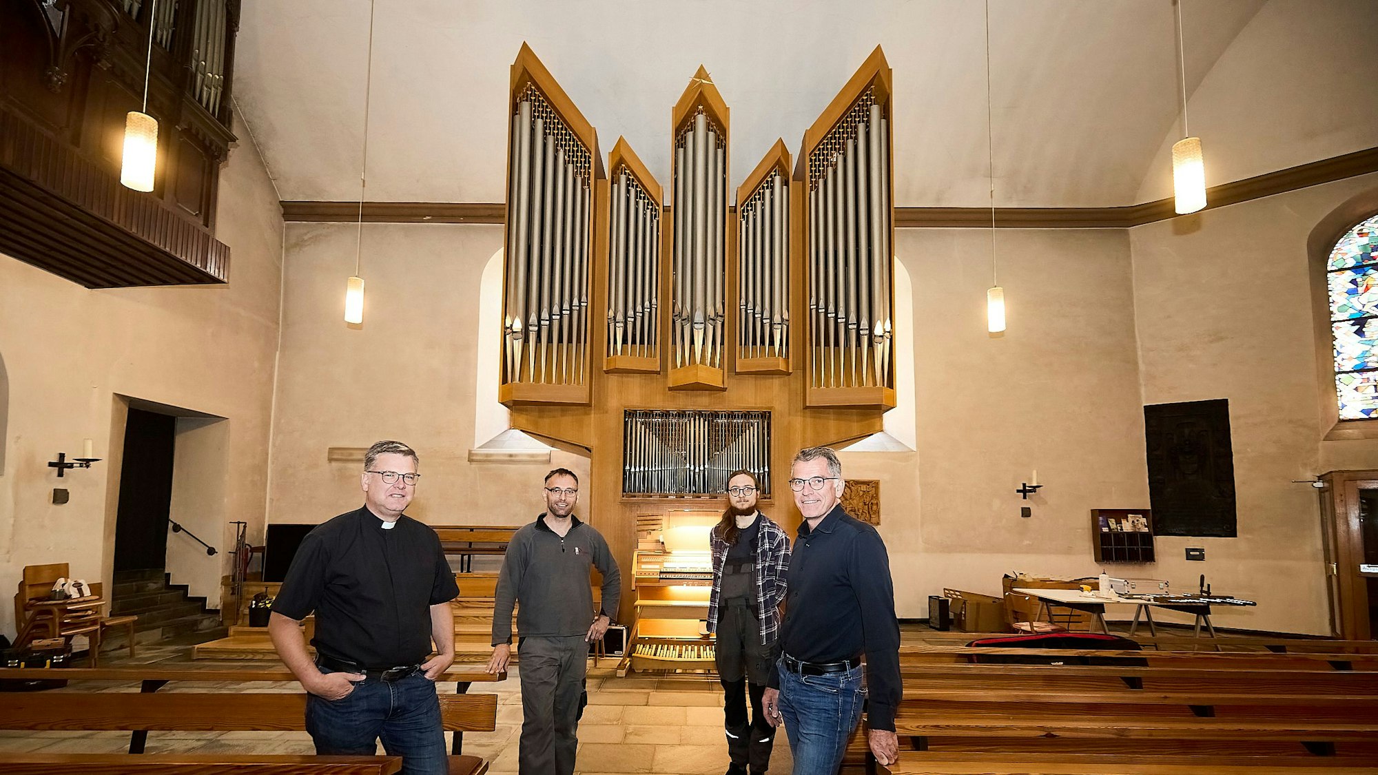 Andreas Züll, Markus Moutschen, ein Auszubildender und Frank Weimbs (v.l.) stehen vor der Kirche, im Hintergrund sind Orgelpfeifen zu sehen.
