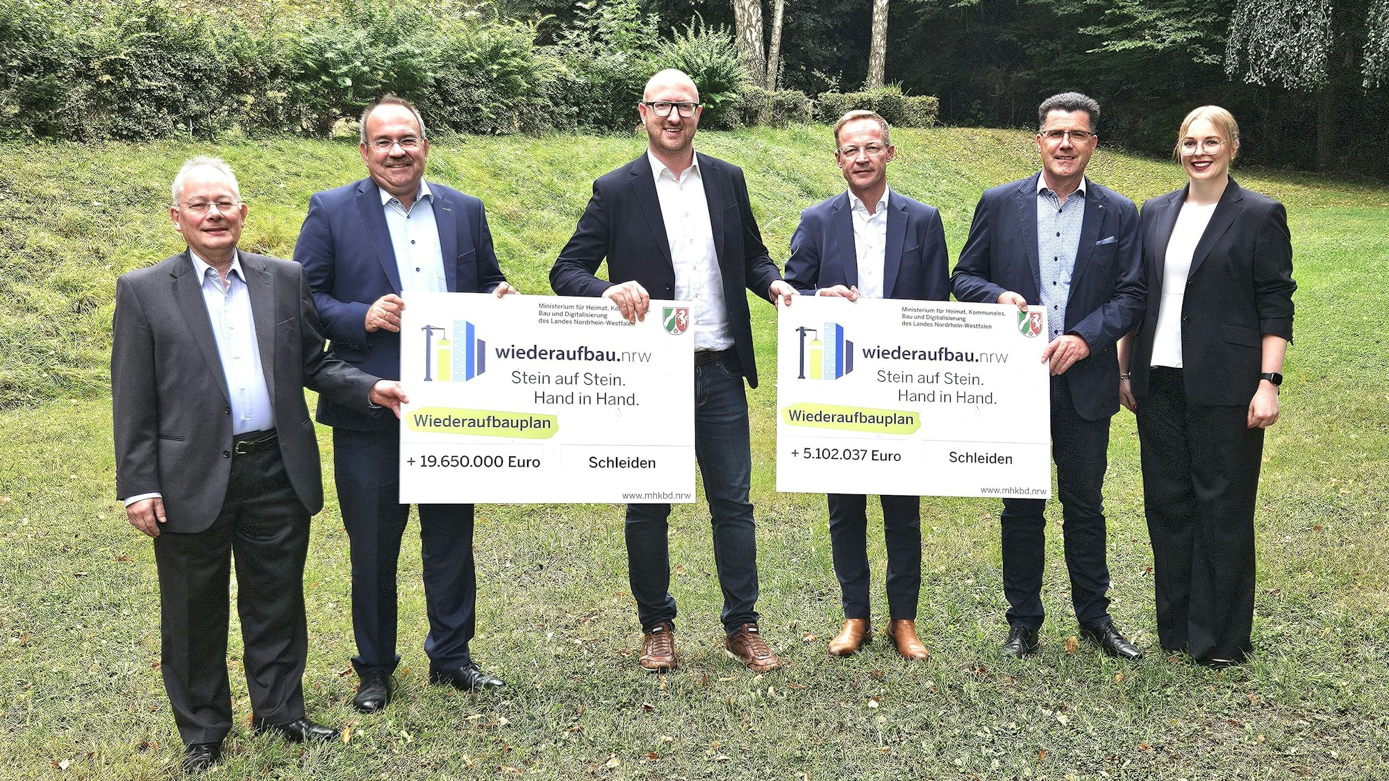 Fünf Männer und eine Frau stehen nebeneinander und präsentieren die beiden symbolischen Förderbescheide.