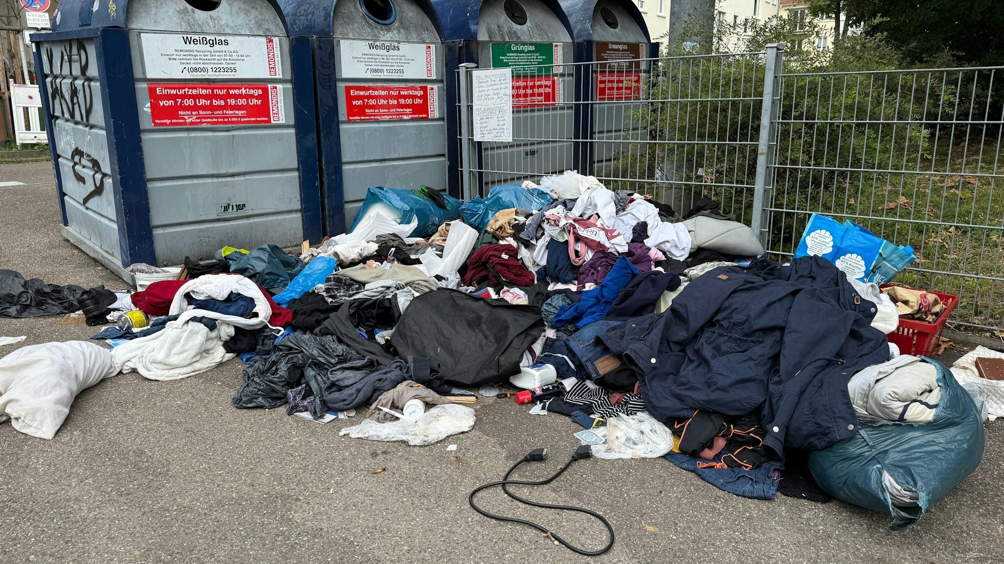 PRODUKTION - 03.09.2025, Baden-Württemberg, Stuttgart: Altkleider und Abfall liegen vor Altglascontainern in der Nähe eines Spielplatzes.