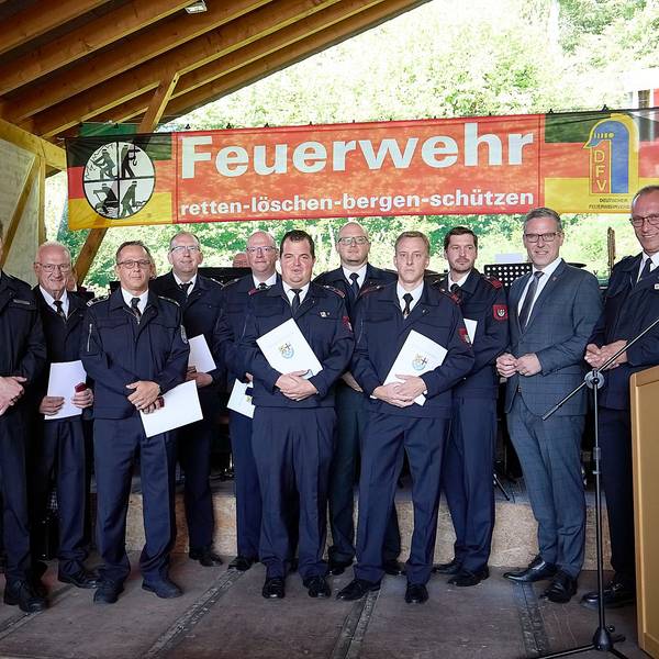 Die geehrten Feuerwehrleute haben sich vor einer Feuerwehr-Fahne zum Gruppenbild zusammengestellt.