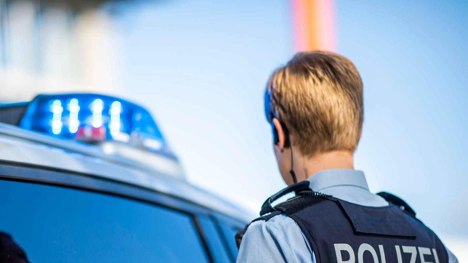 Eine Polizistin steht vor einem Streifenwagen, dessen Blaulicht leuchtet. (Symbolbild)