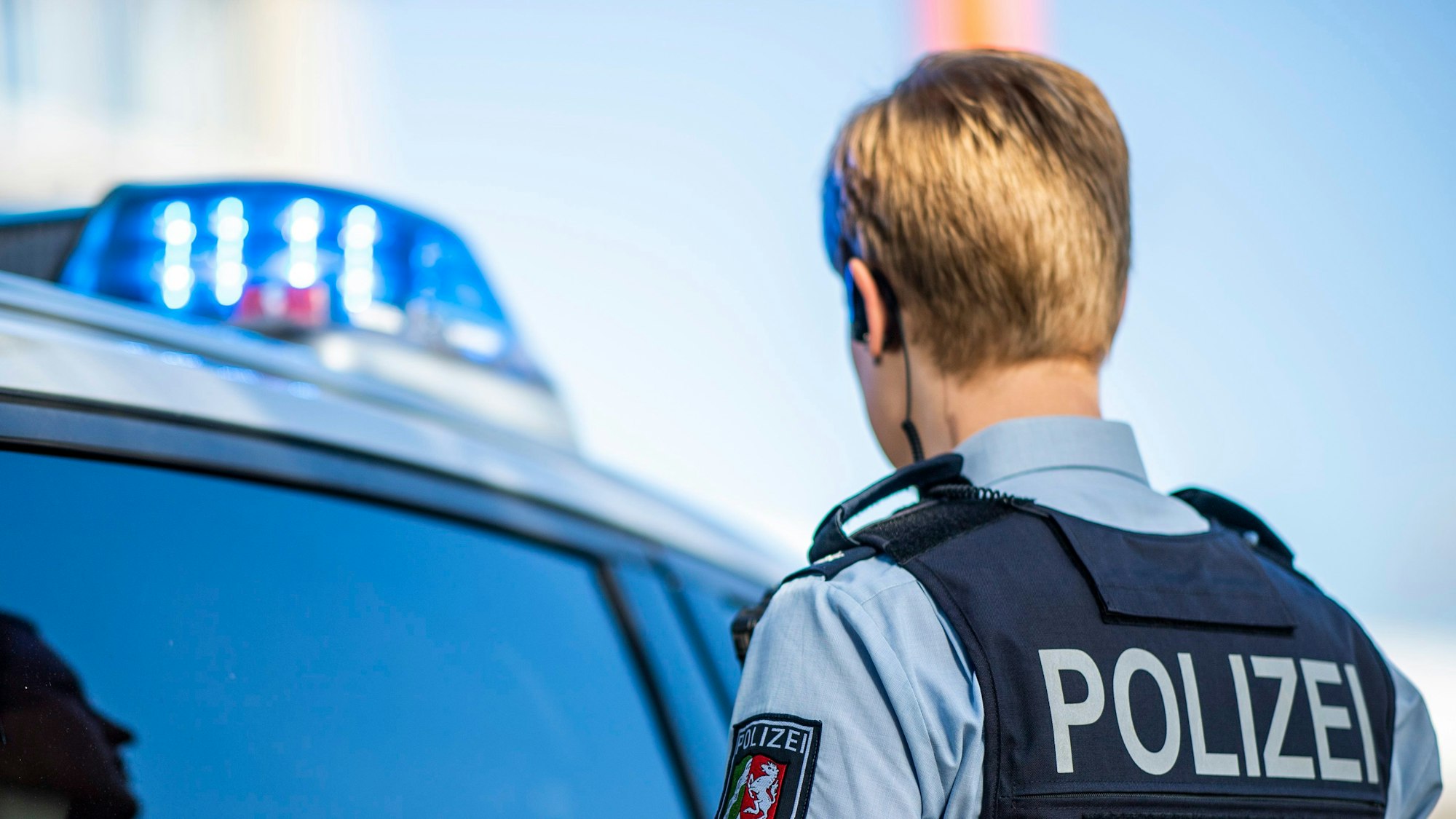 Eine Polizistin steht vor einem Streifenwagen, dessen Blaulicht leuchtet. (Symbolbild)