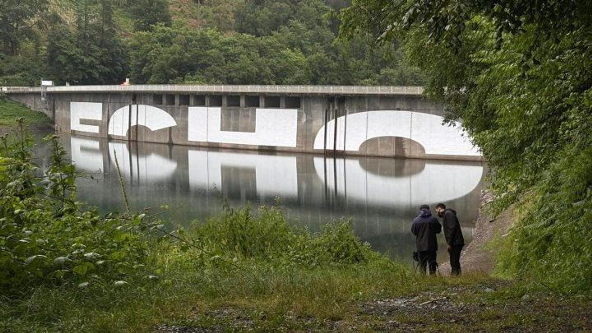 Ein Schriftzug an der Staumauer der Aggertalsperre bei Gummersbach spiegelt sich im Wasser, so wird der Schriftzug „ECHO“ lesbar.