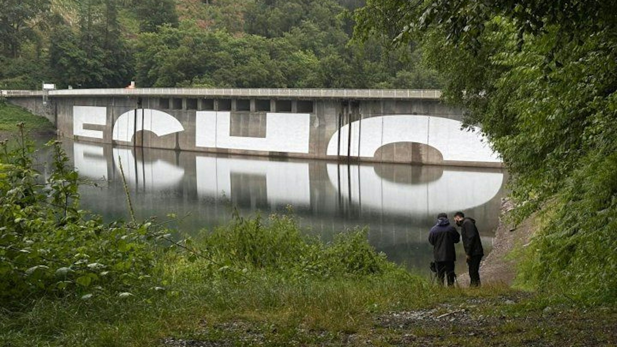 Ein Schriftzug an der Staumauer der Aggertalsperre bei Gummersbach spiegelt sich im Wasser, so wird der Schriftzug „ECHO“ lesbar.