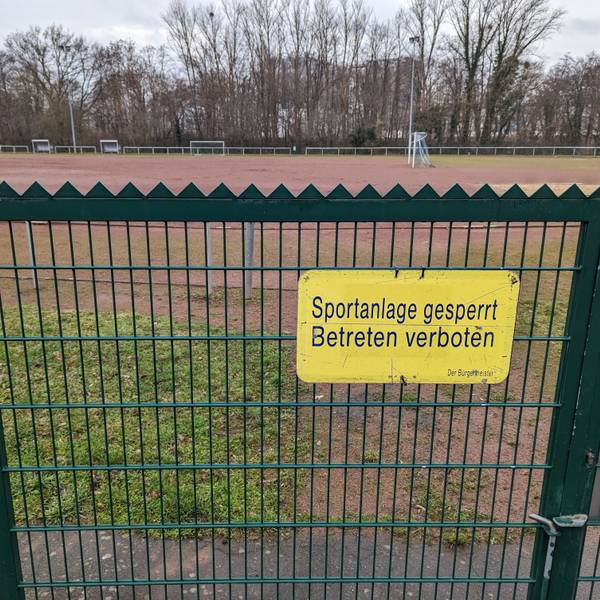 Das Foto zeigt ein Schild „Sportanlage gesperrt. Betreten verboten“ am Tor zum Tennenplatz an der Buschstraße.