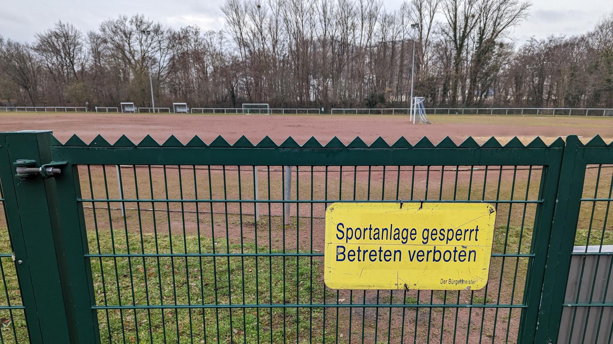 Das Foto zeigt ein Schild „Sportanlage gesperrt. Betreten verboten“ am Tor zum Tennenplatz an der Buschstraße.