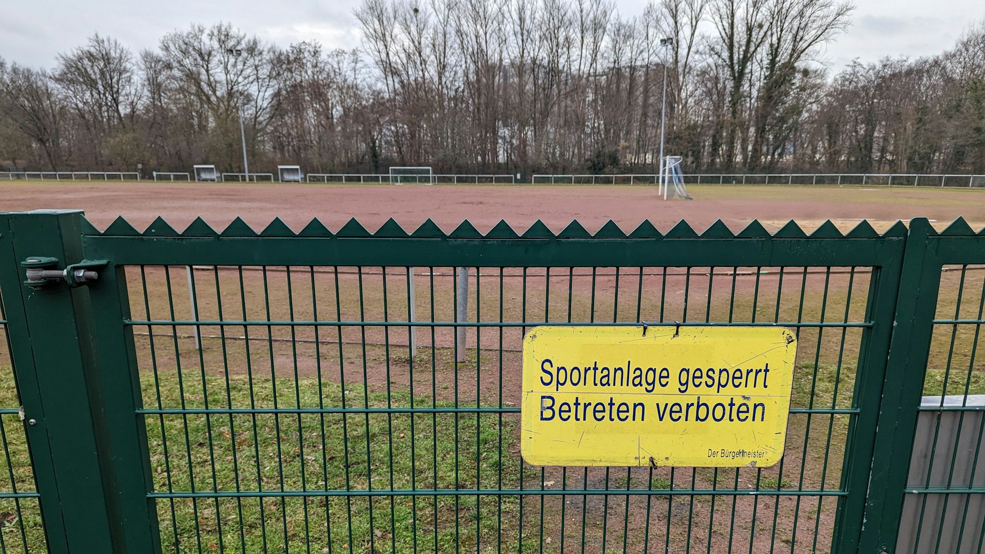 Das Foto zeigt ein Schild „Sportanlage gesperrt. Betreten verboten“ am Tor zum Tennenplatz an der Buschstraße.