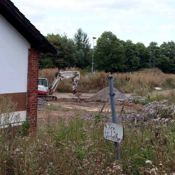 Der Sportplatz in Bad Münstereifel besteht aus Geröllhaufen und ist zugewuchert. Im Hintergrund steht ein Bagger, im Vordergrund ist das schon vor der Flut nicht mehr nutzbare Vereinsheim zu sehen, daneben steht ein Schild mit dem Hinweis „Kein Winterdienst“.