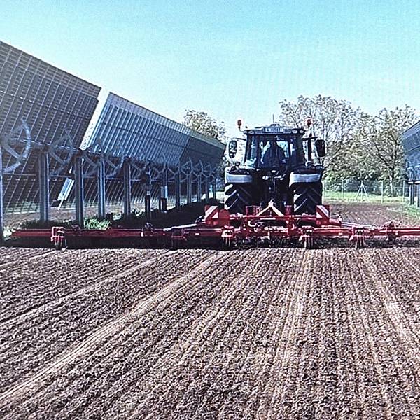 Ein Traktor mit angehängter Maschine fährt zwischen zwei Modulreihen hindurch.
