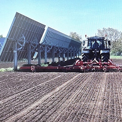 Ein Traktor mit angehängter Maschine fährt zwischen zwei Modulreihen hindurch.