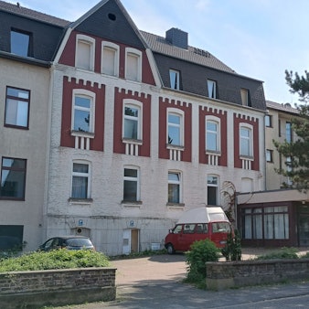 Zu sehen ist das mehrstöckige Haus, davor parken zwei Autos.