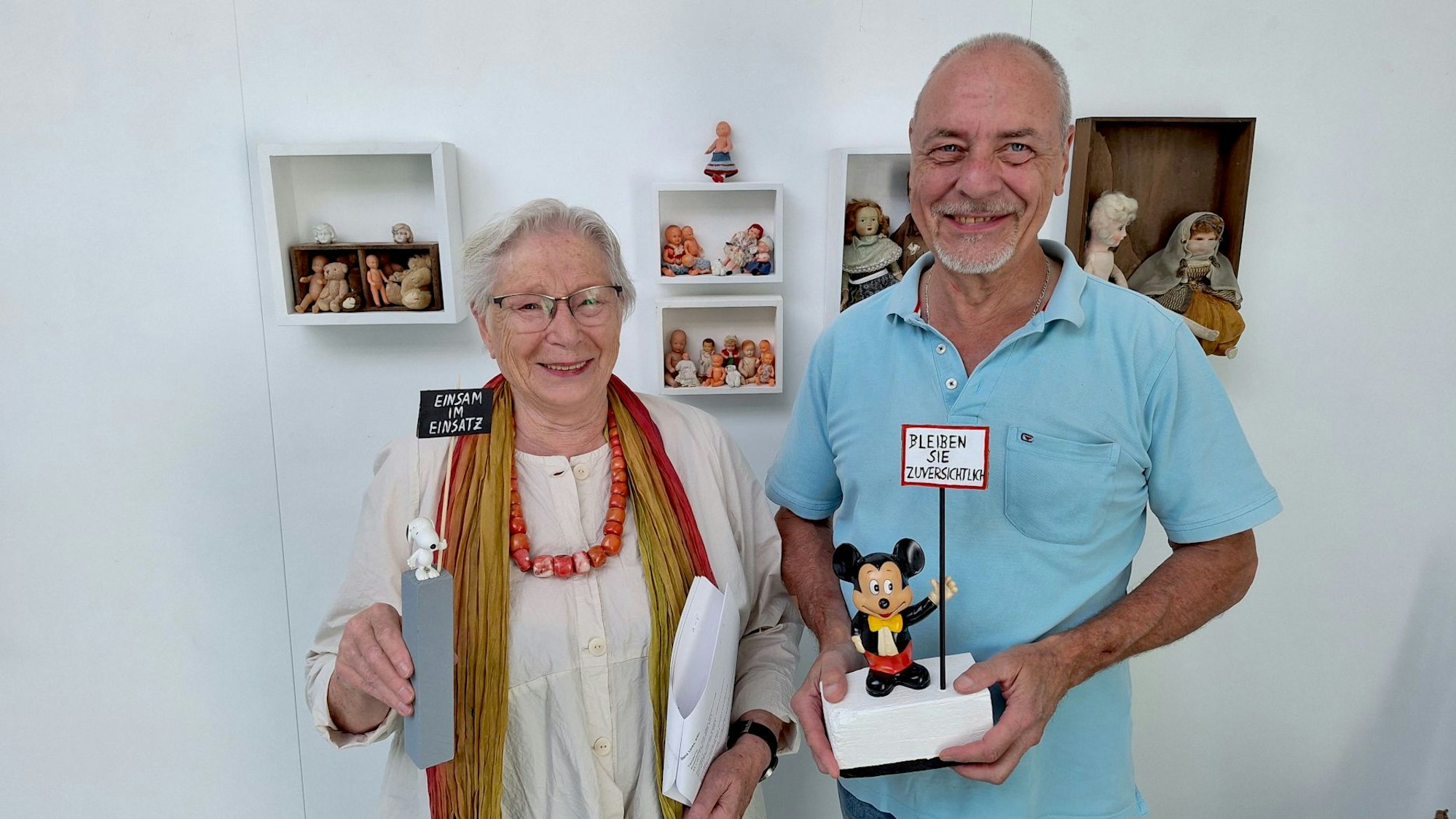 Die Kuratorin und der Geschäftsführer stehen vor Wandkästen und halten Ausstellungsstücke in den Händen.